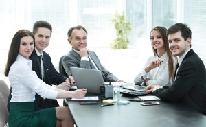 Team members at conference table with laptop smiling at camera